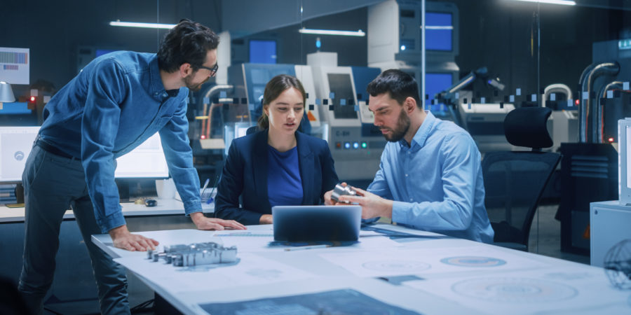 Three people are talking about a object on a desk at work